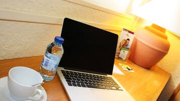 Ein Laptop auf einem Holztisch, neben ihm eine weiße Tasse und eine Wasserflasche.