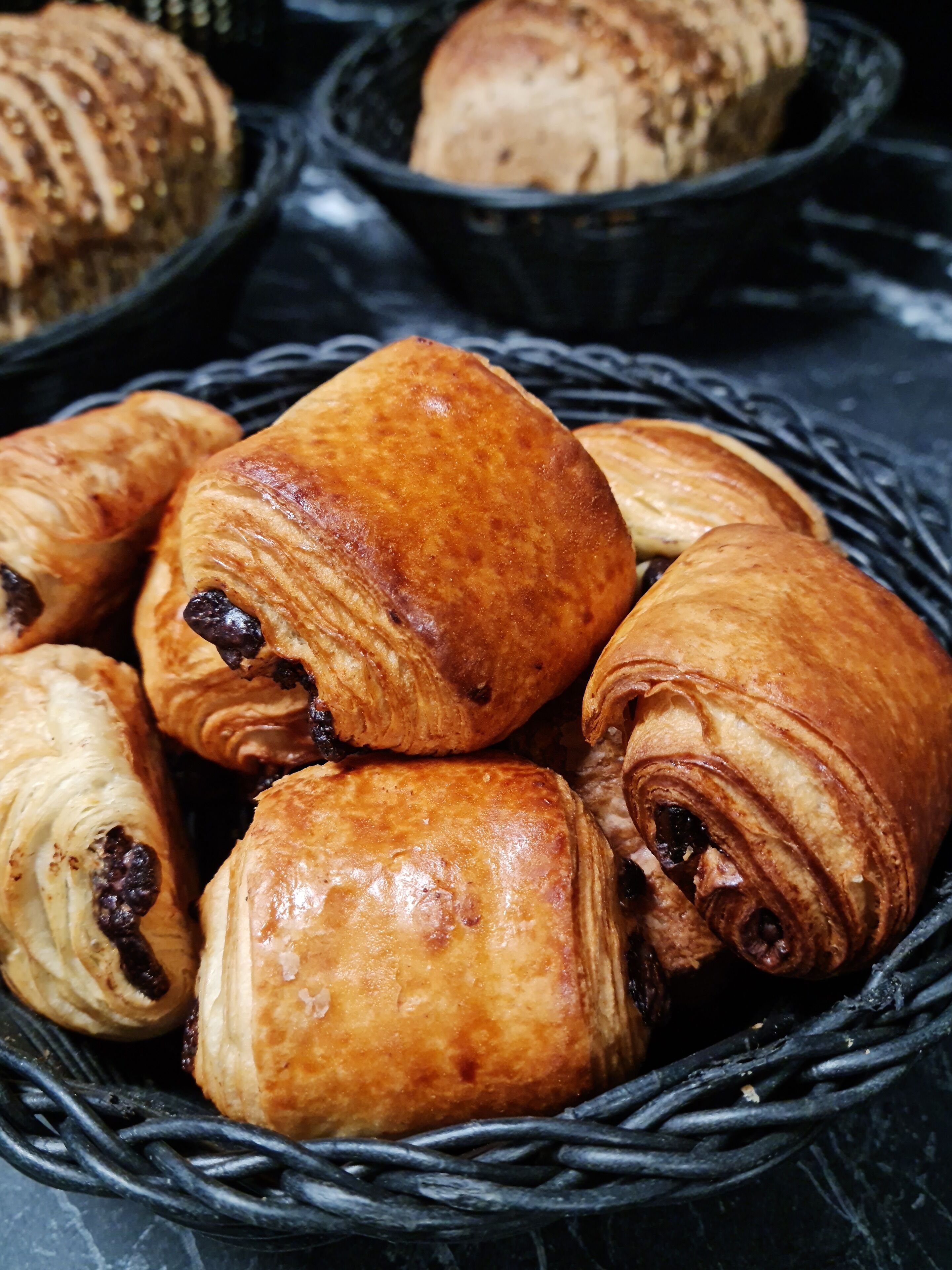 A basket filled with various types of pastries, including croissants and chocolate-filled rolls.