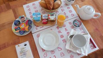 Una mesa de desayuno con cruasanes, yogur, jugo y una tetera.