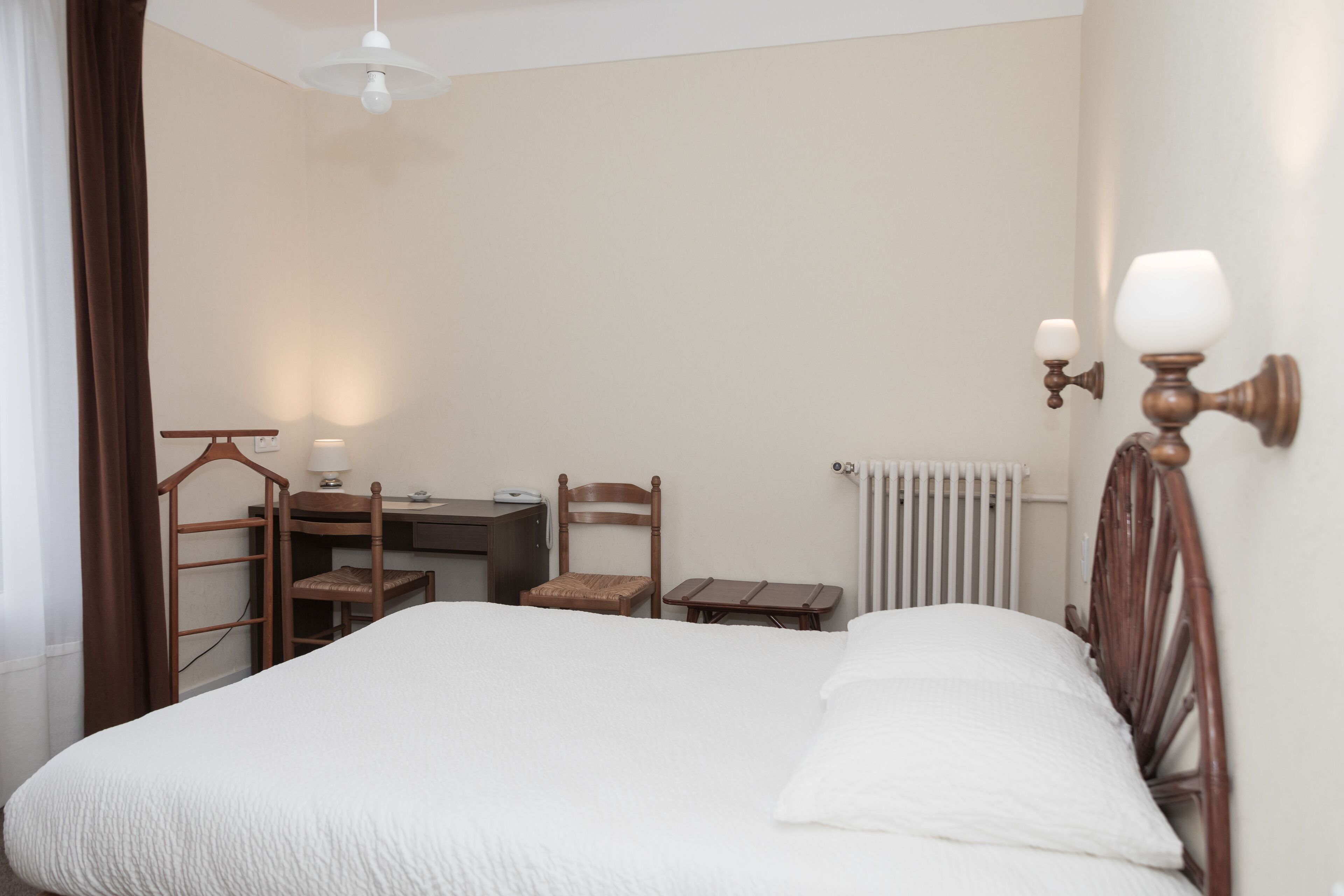 A bedroom with a bed, a desk, a chair, and a radiator.