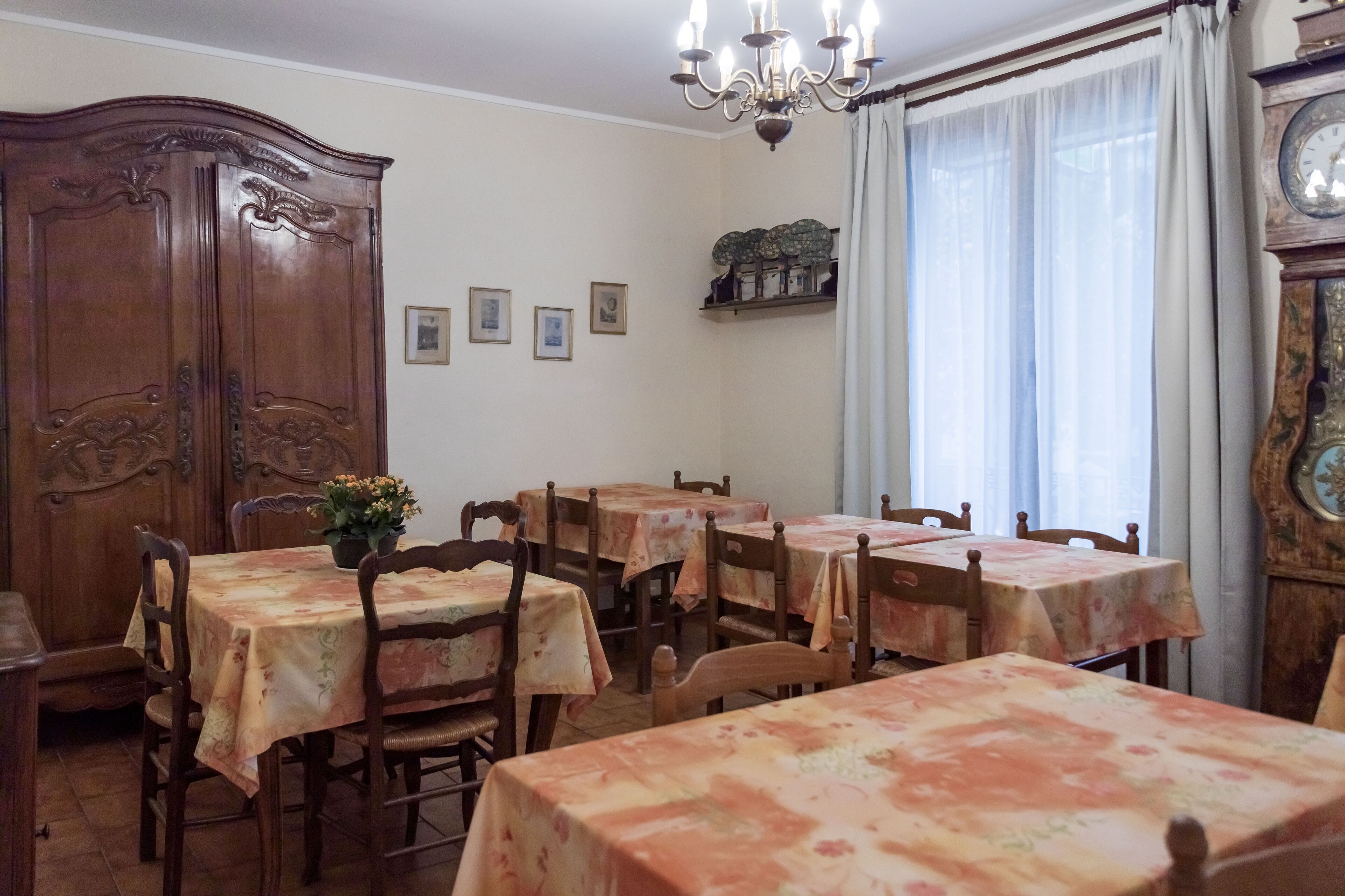 A dining area with multiple tables and chairs, a wooden cabinet, and a chandelier.