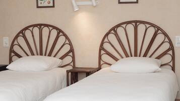 Dos camas individuales con cabeceros de madera, mesitas de noche pequeñas y lámparas fijadas a la pared.