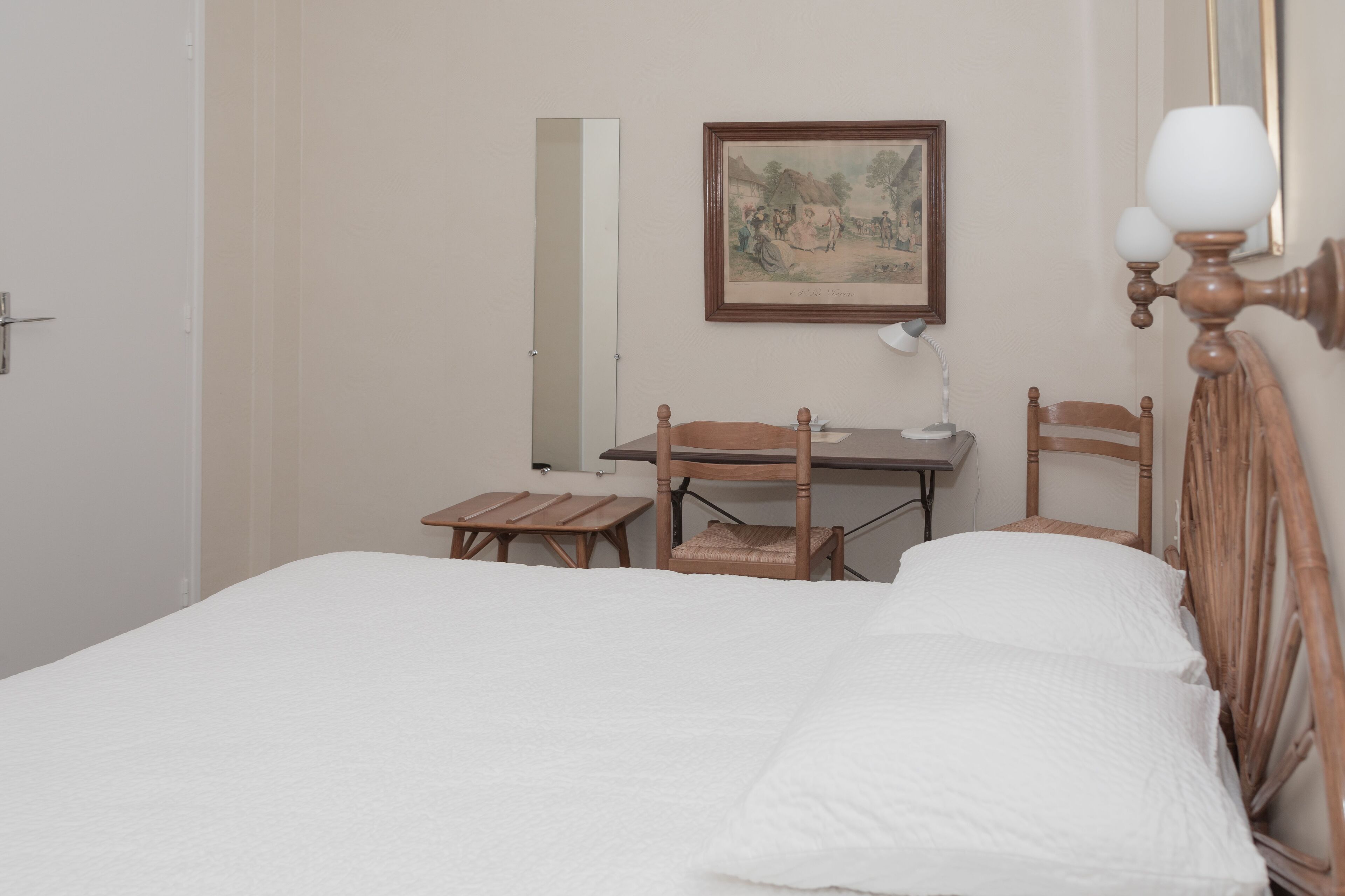 A bedroom with a bed, a desk, two chairs, a lamp, and a framed picture on the wall.
