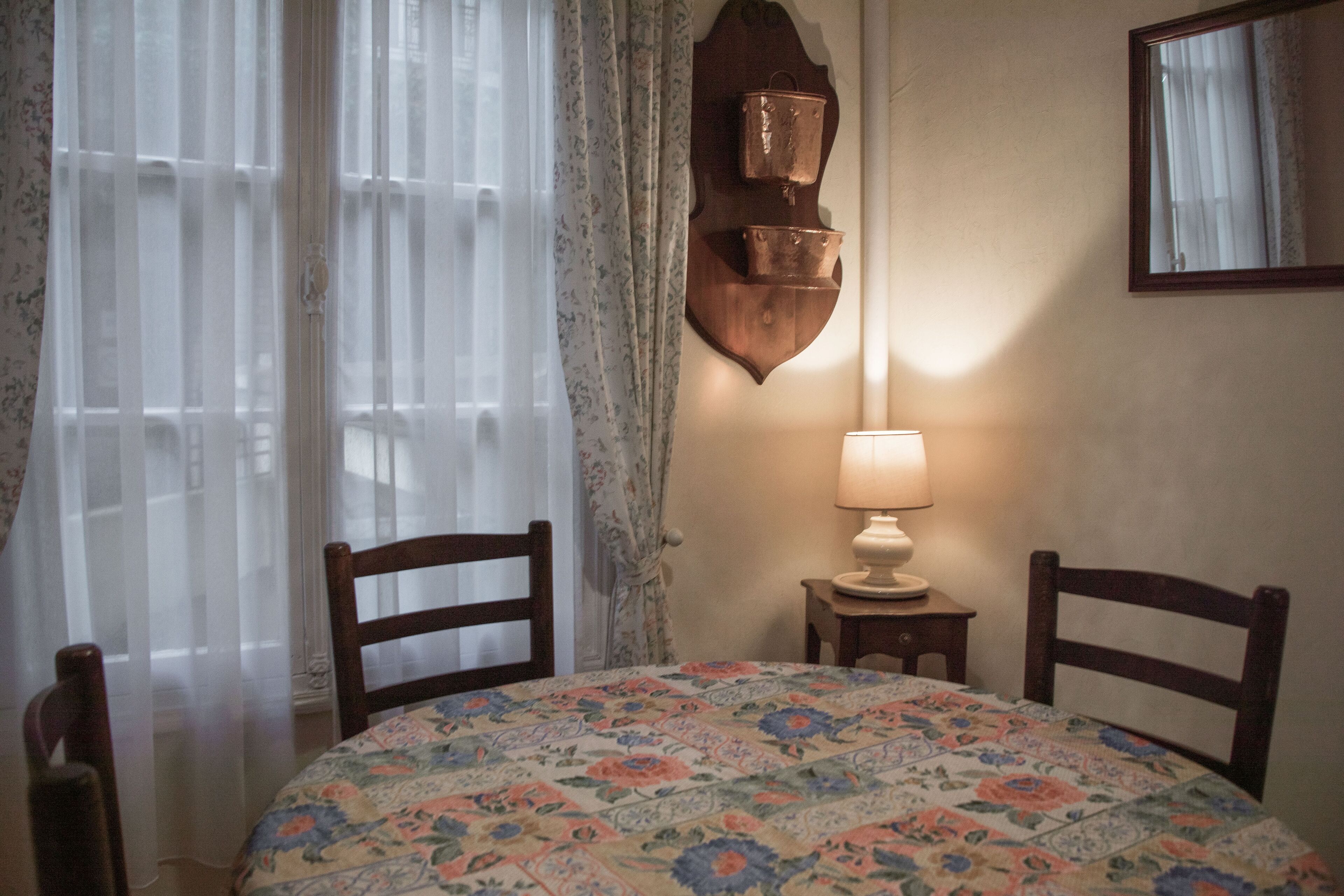 A room with a round table, two chairs, a lamp, and a wall-mounted shelf with a copper pot.