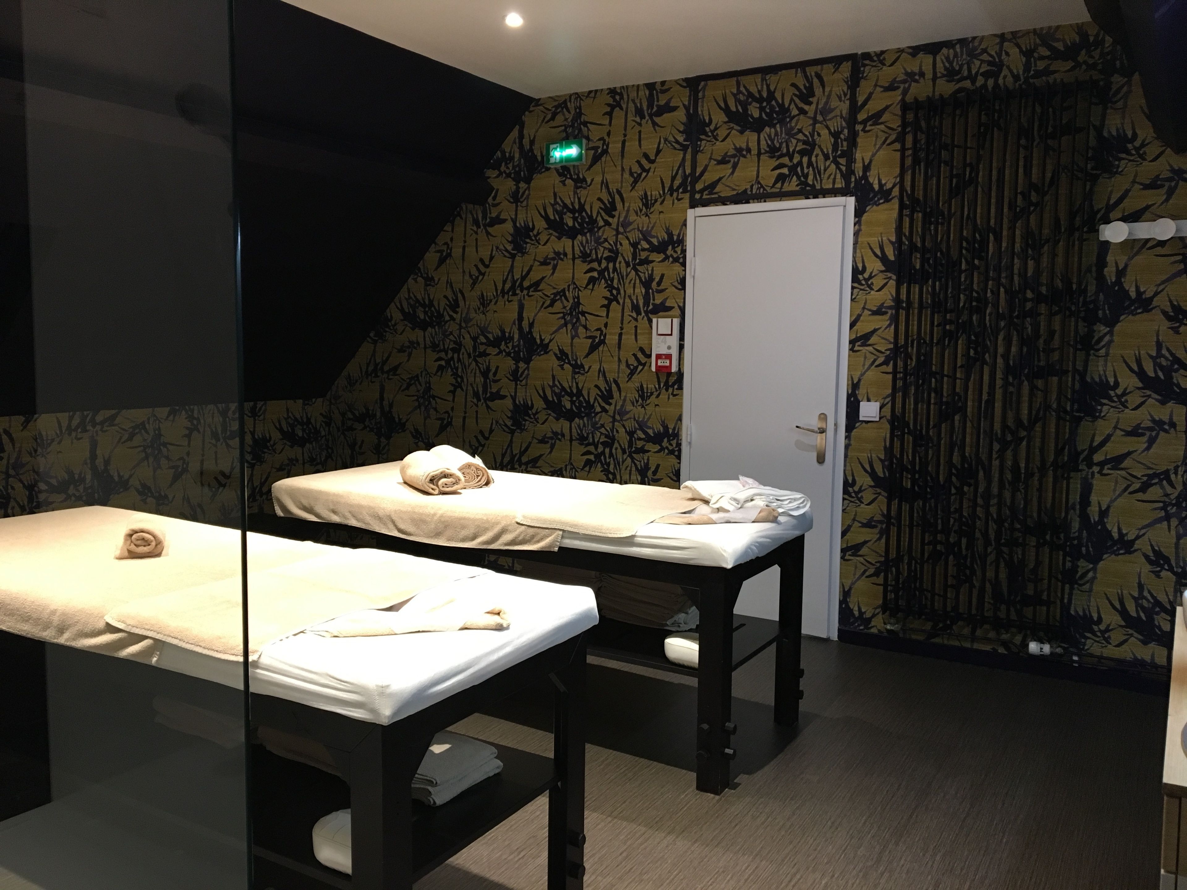 A room with two massage tables, a door, and a patterned wall.