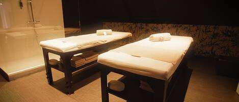 Two massage tables with towels, a glass shower enclosure, and a bamboo-patterned wall.