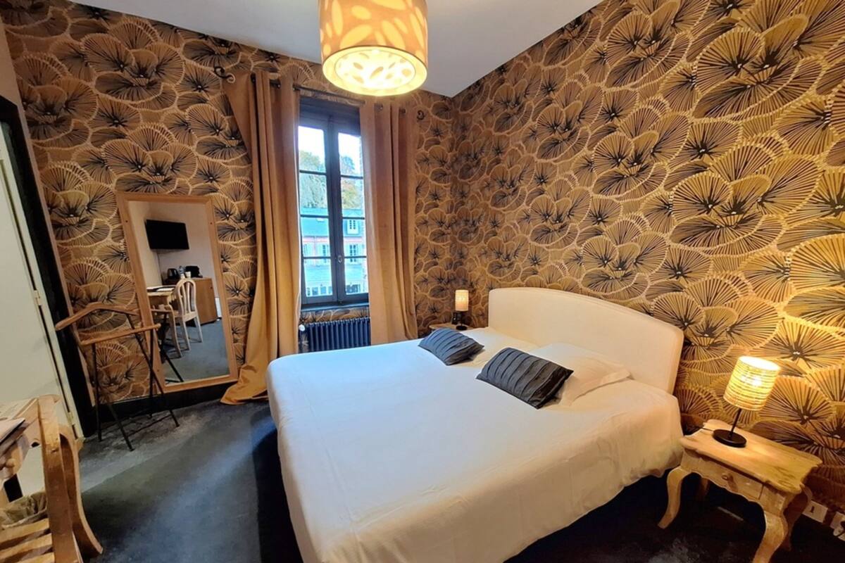 A hotel room with a large bed, a mirror, a window, and a patterned wall.