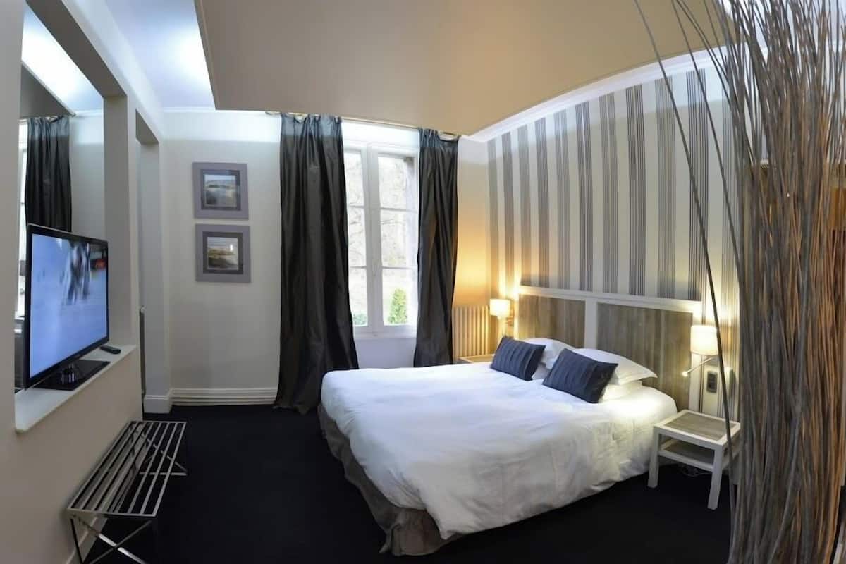 A hotel room with a large bed, a television on a stand, a small bedside table, and a window with curtains.