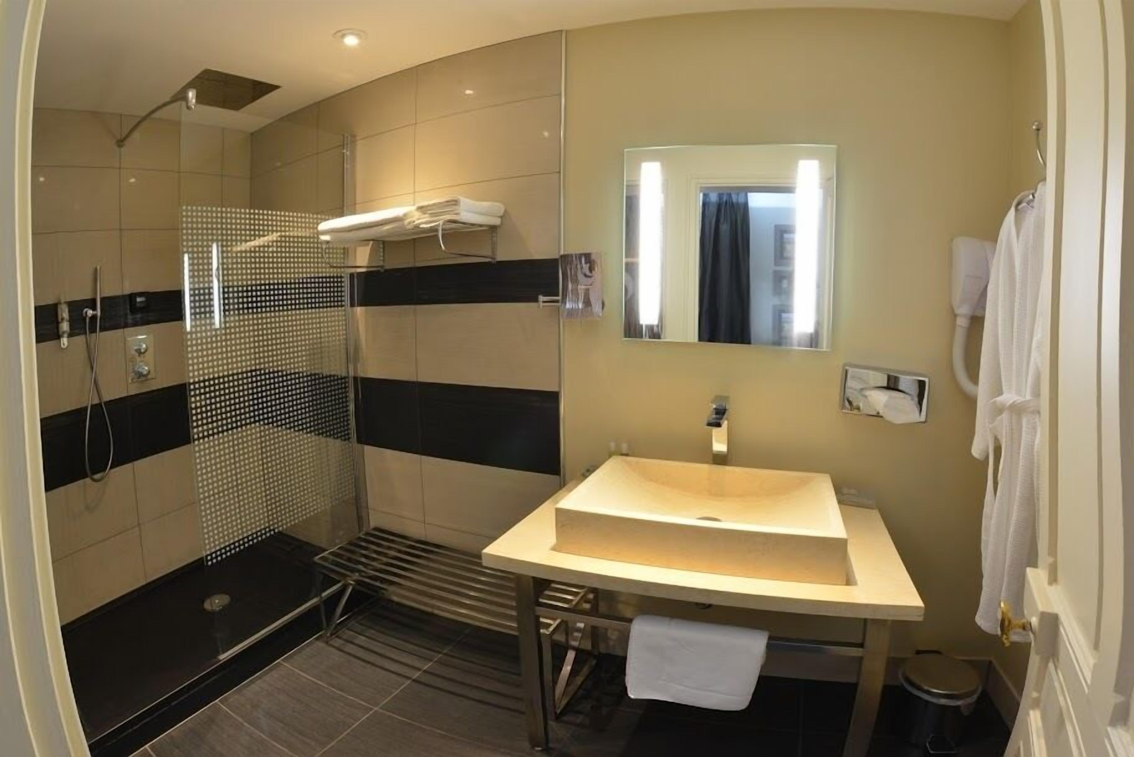Un baño moderno con ducha envuelta en vidrio, lavamanos con espejo y perchero para toallas.