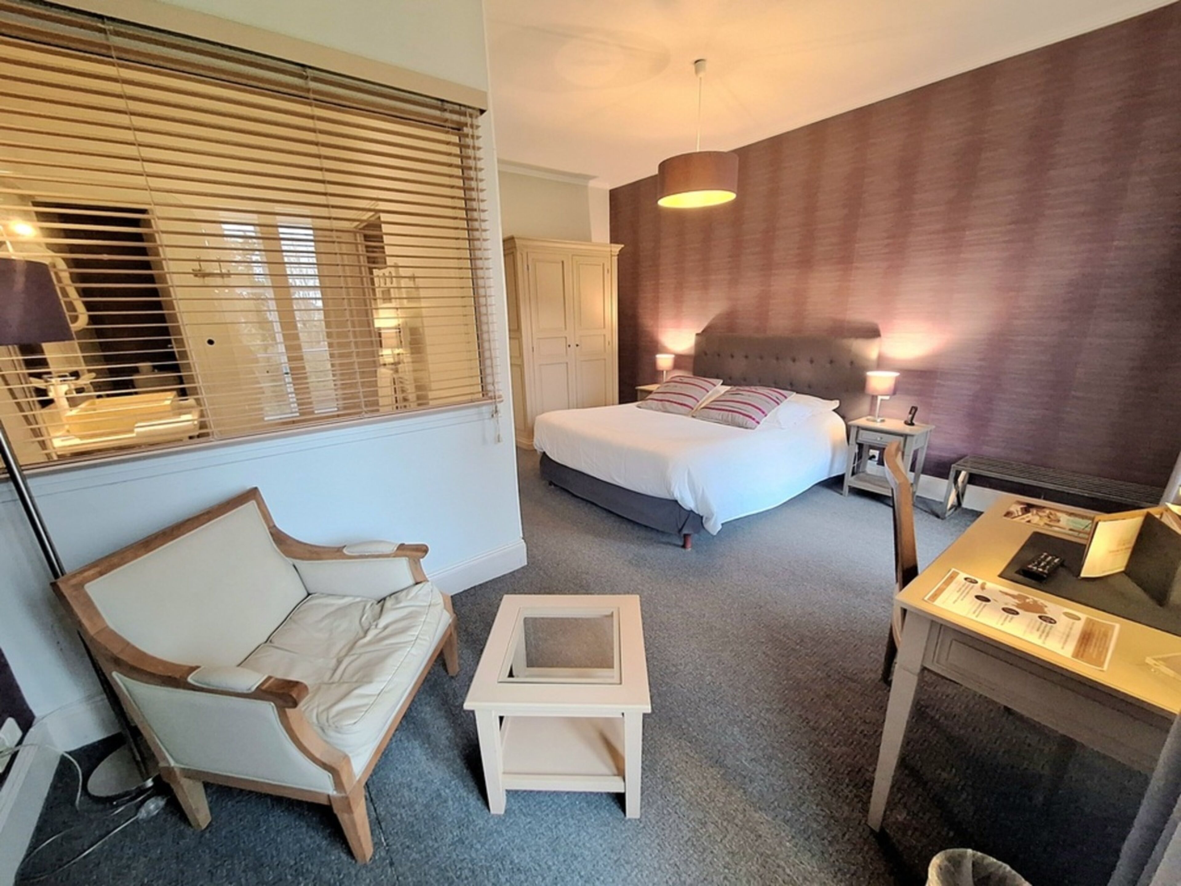 A hotel room with a bed, a chair, a small table, and a desk.