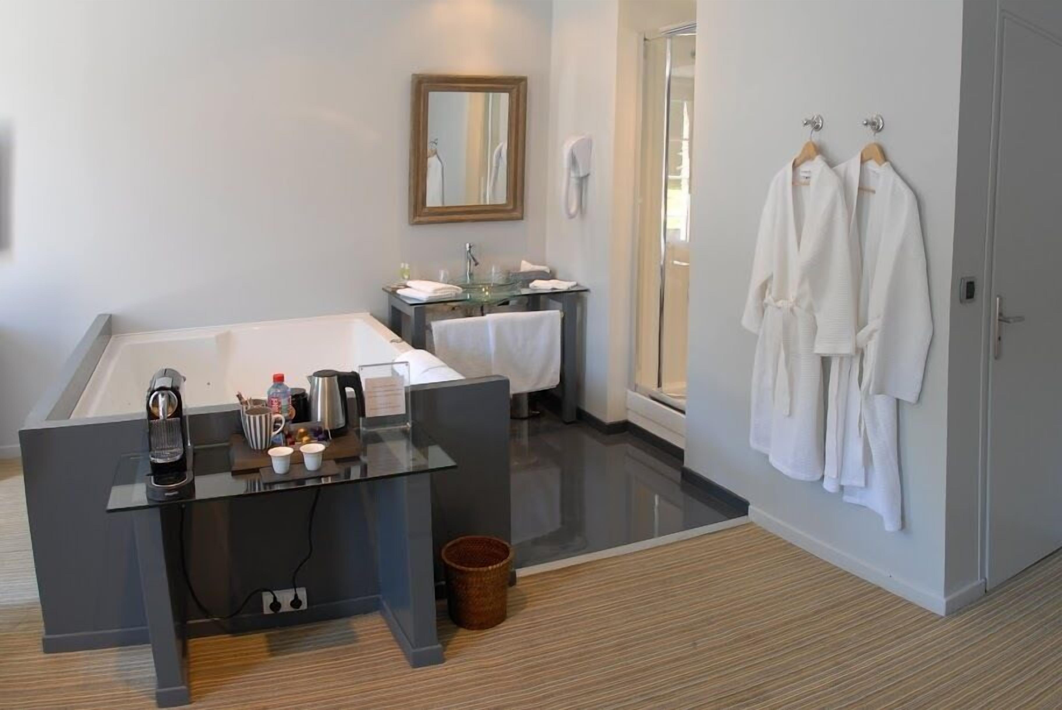 A modern bathroom with a large bathtub, a glass vanity, and two white robes hanging on the wall.