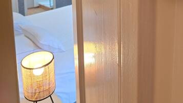 Een houten bord met de tekst 'COCO CHANEL', een bed met wit beddengoed en een lamp met een geweven kap.