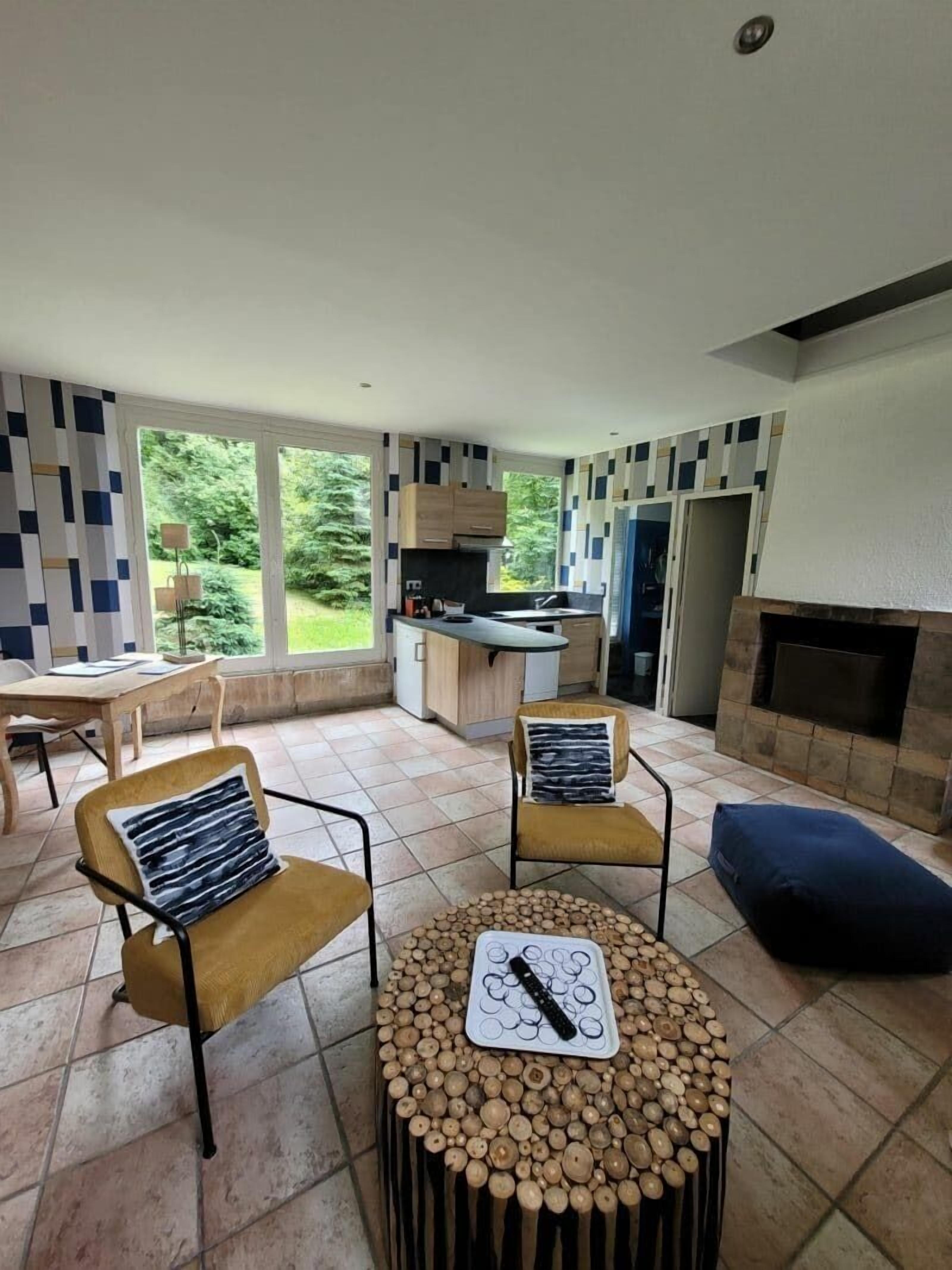A modern living room with a fireplace, two armchairs, a coffee table, and a kitchen in the background.