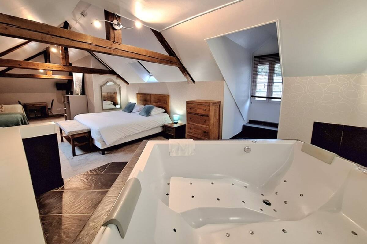 A bedroom with a large bed, a wooden dresser, a nightstand, and a bathroom with a bathtub.
