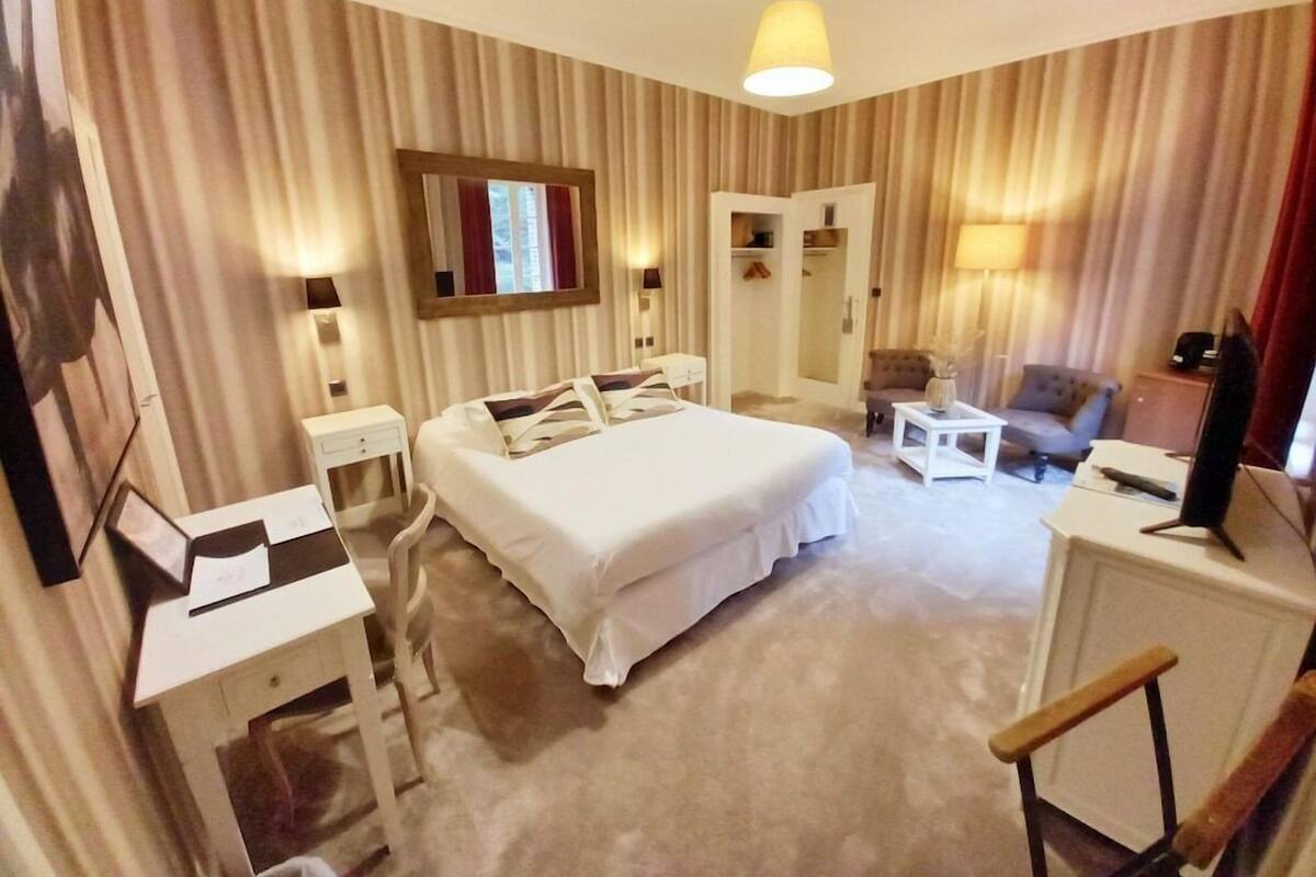 A hotel room with a bed, bedside tables, a desk, a chair, a sofa, and a TV.