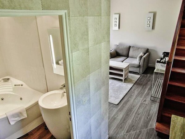 A modern bathroom with a bathtub, sink, and a mirror. There is a living area with a sofa and a coffee table. - Domaine de Joinville & Spa (Eu)