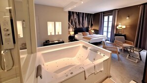 A modern hotel room with a large bathtub, a bed, a desk, and a chair. - Domaine de Joinville & Spa (Eu)