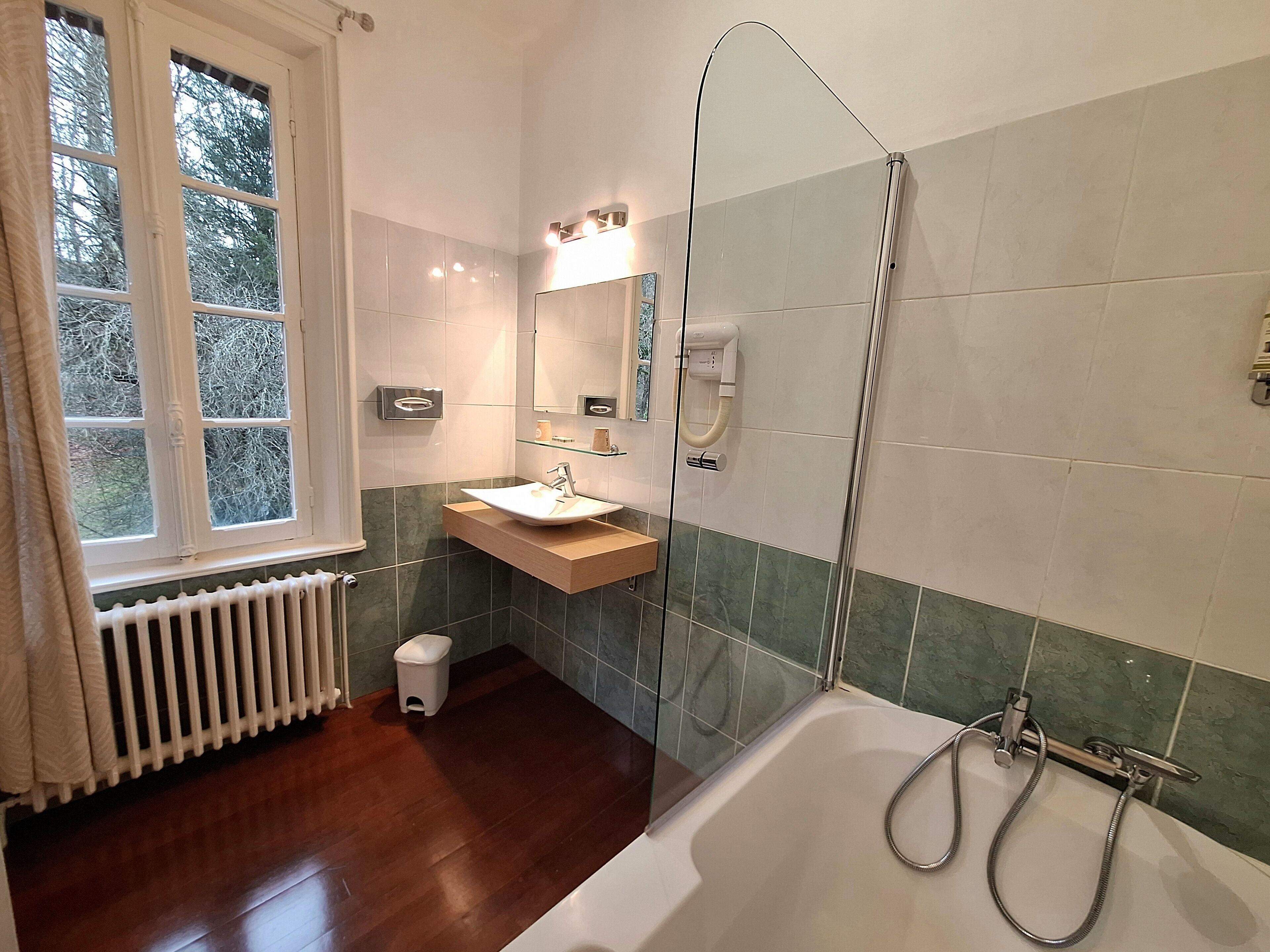 Une salle de bain équipée d’une baignoire, d’un lavabo, d’une cabine de douche en verre, d’une fenêtre et d’un radiateur.