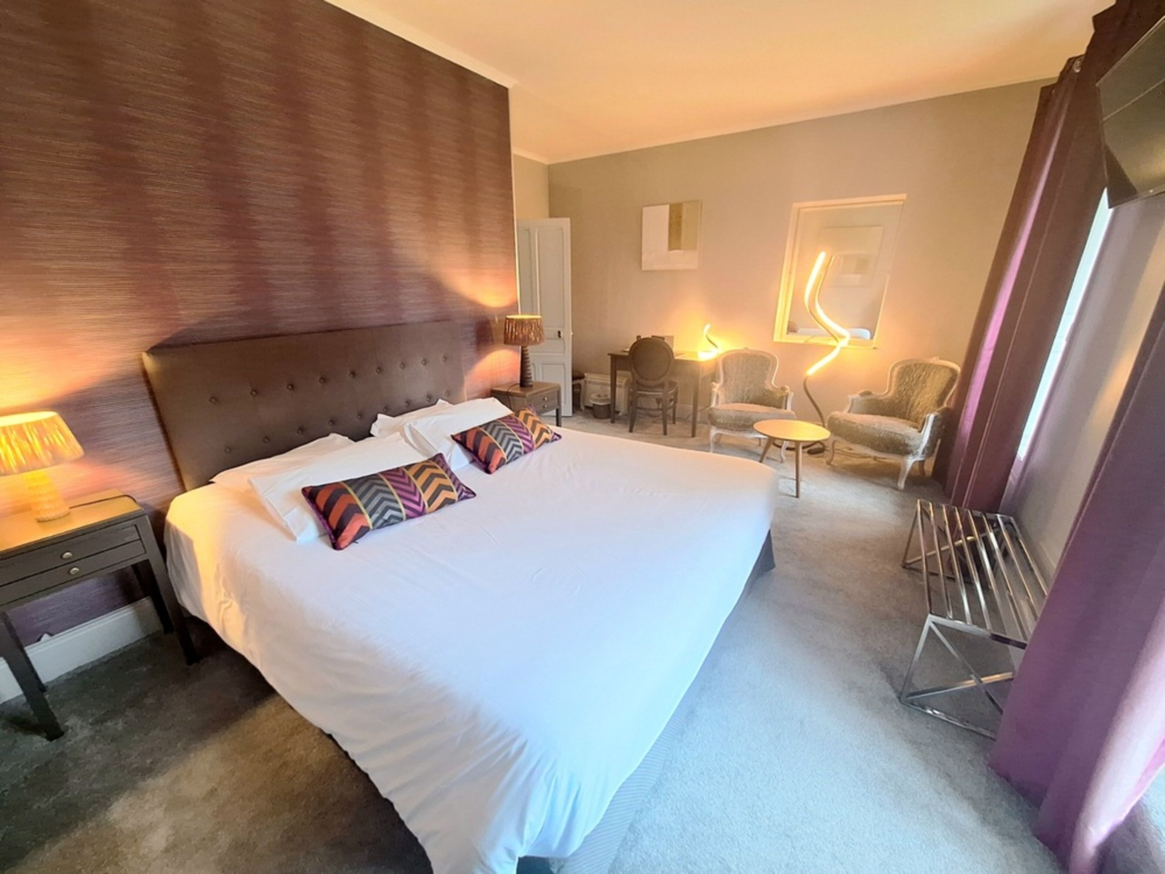 Habitación de hotel con una cama grande, una mesita de noche, un escritorio, dos sillones y una pequeña mesa.