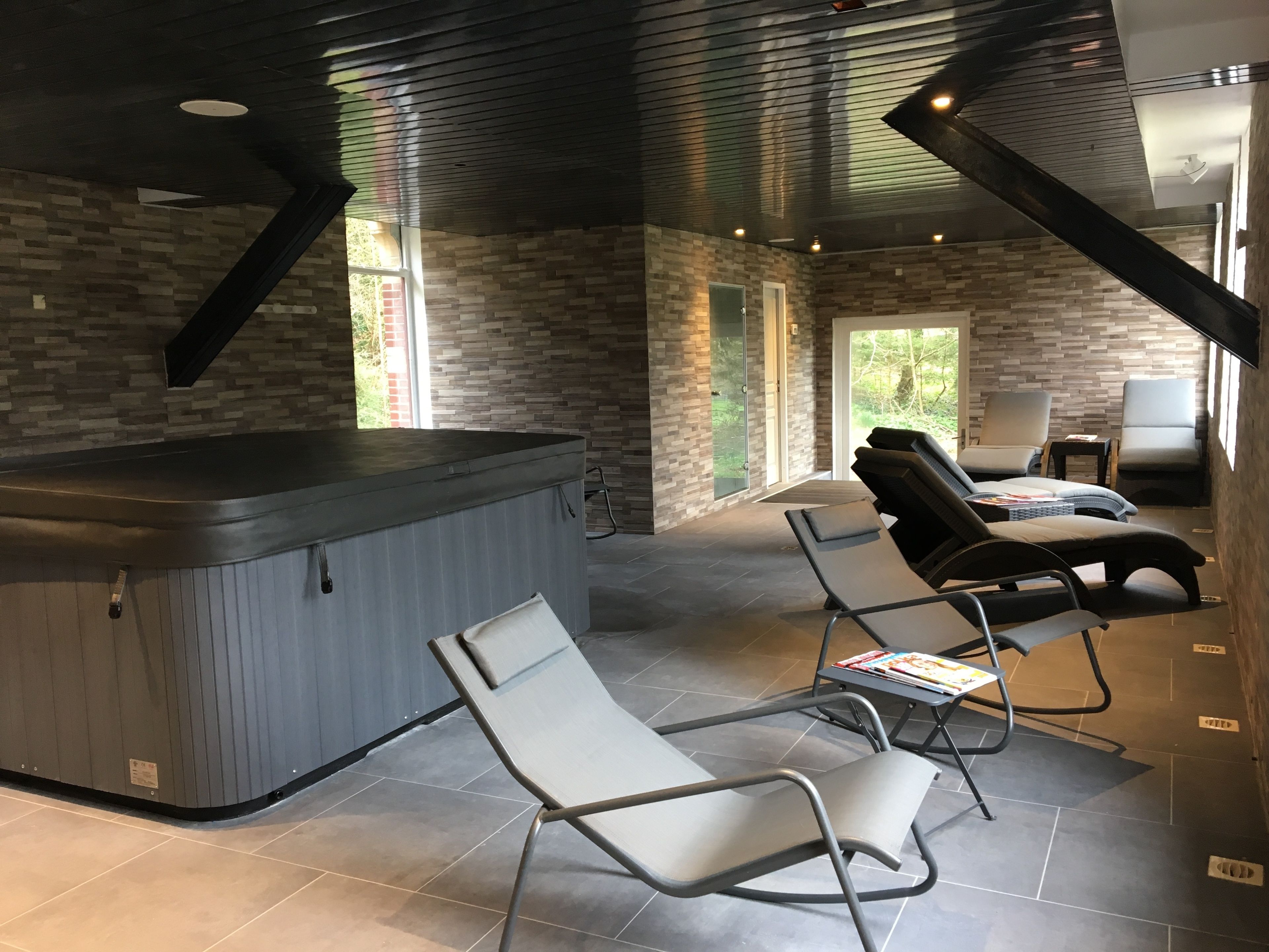 A modern spa area with a hot tub, lounge chairs, and a stone wall.