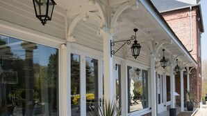 A covered patio area with large windows, potted plants, and hanging lanterns. - Domaine de Joinville & Spa (Eu)