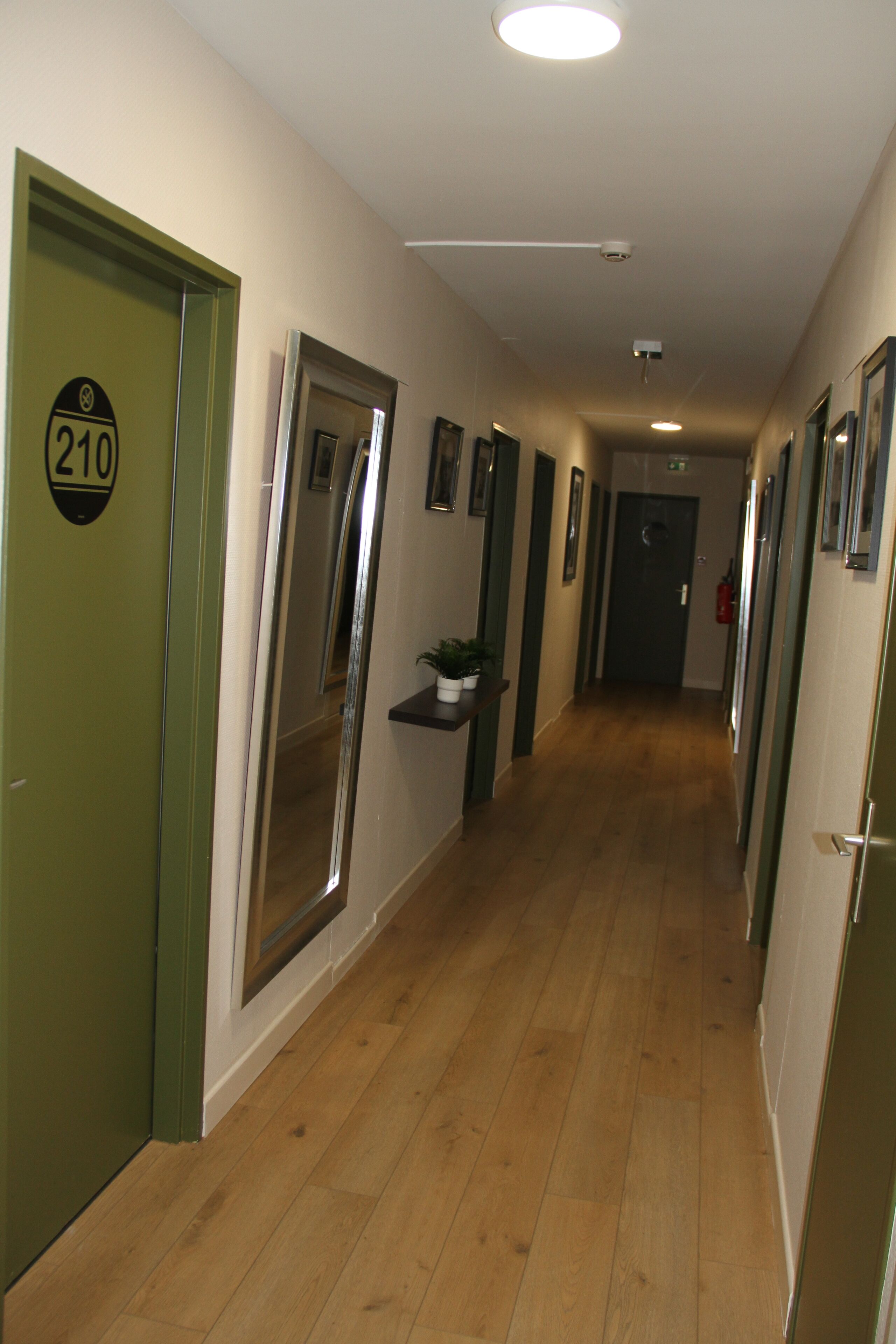 A hallway with wooden flooring, green doors, and a number sign on one door.
