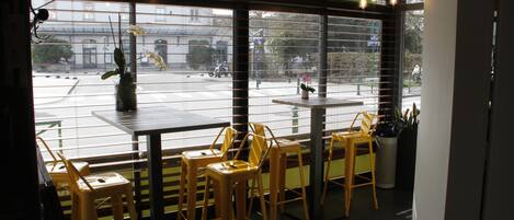 An indoor seating area with tables and chairs, large windows, and hanging light bulbs.