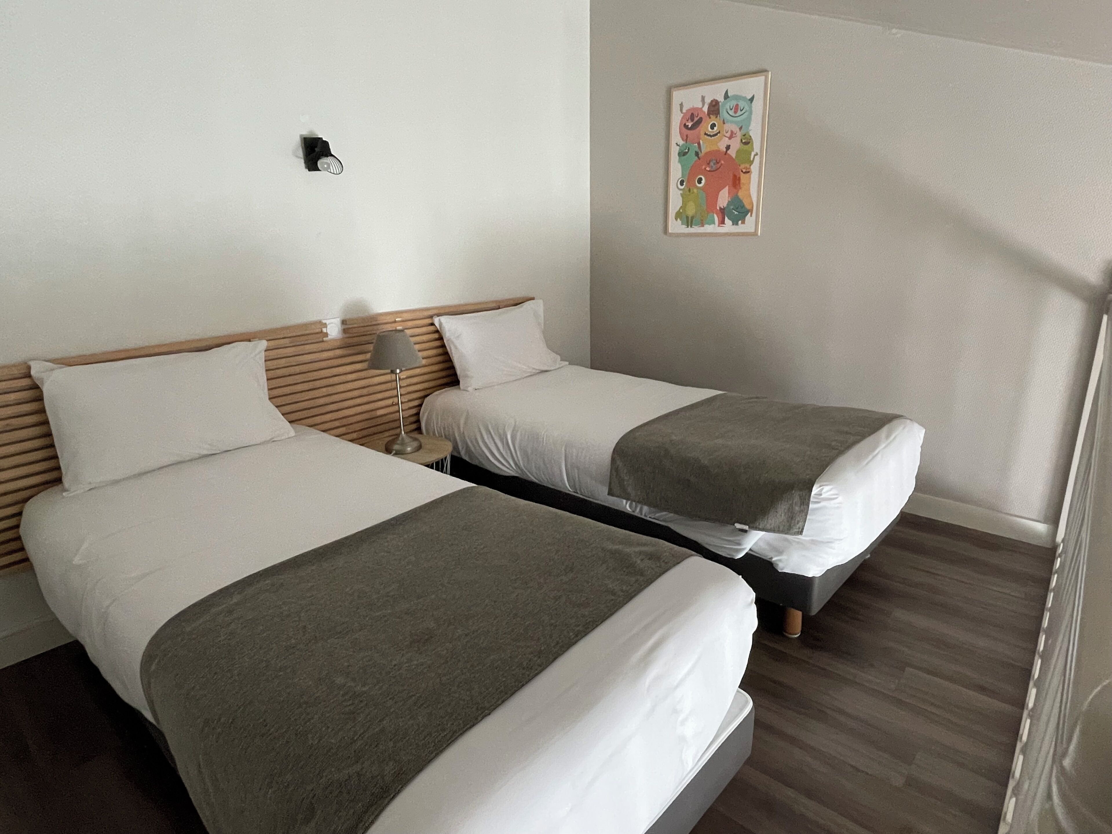 Una habitación de hotel con dos camas, una mesita de noche con lámpara y un cuadro enmarcado en la pared.