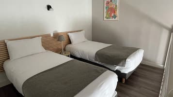 Una habitación de hotel con dos camas, una mesita de noche con lámpara y un cuadro enmarcado en la pared.