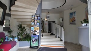 Una escalera de caracol con barandilla blanca, rodeada de plantas en macetas y una exhibición de revistas.