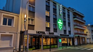 Un hotel con bar y restaurante en la planta baja, que presenta un letrero de neón verde y una fachada moderna.