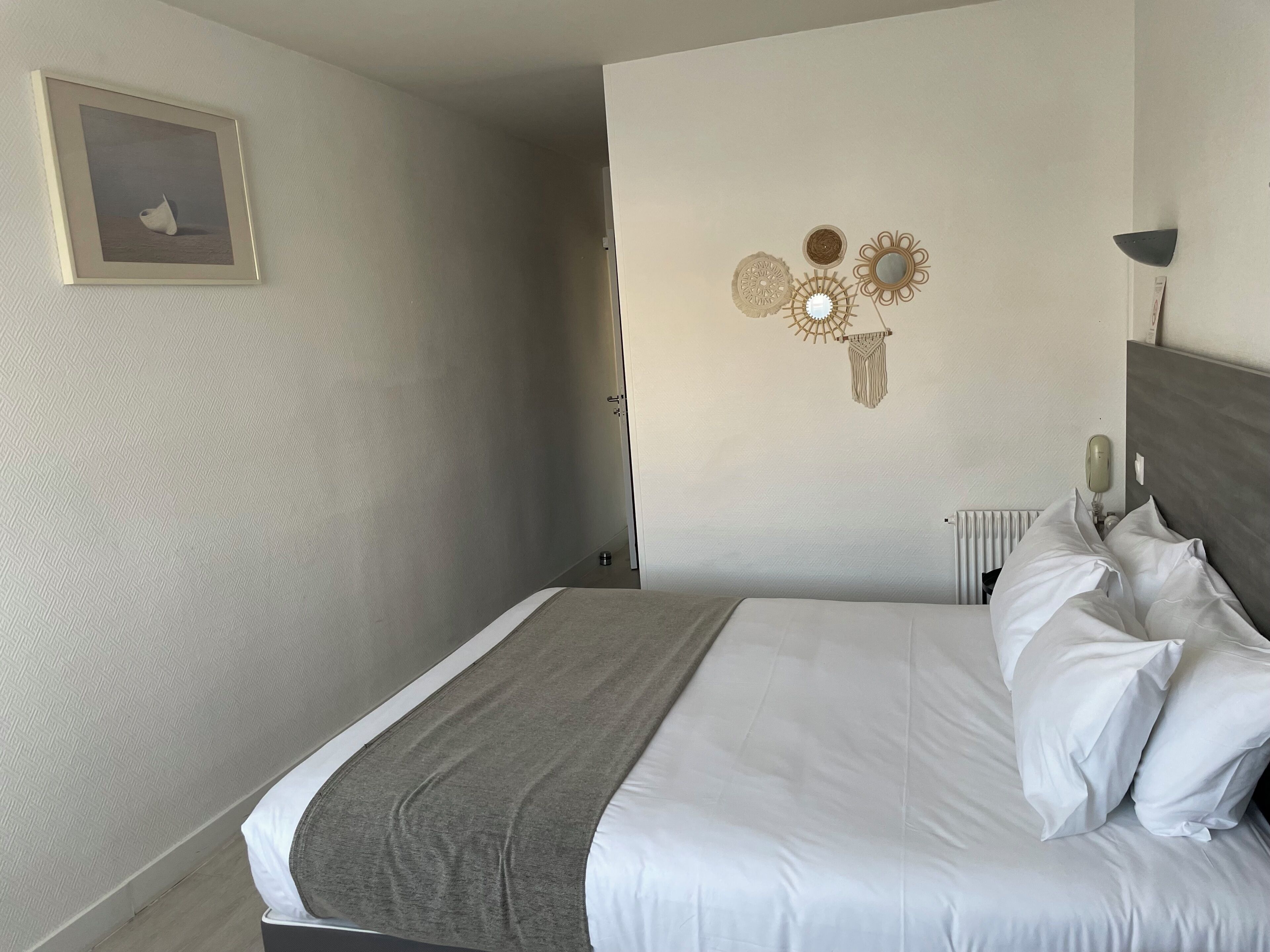 Un letto rifatto con lenzuola bianche e una coperta grigia, un quadro appeso alla parete e decorazioni murali.