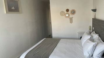 Un letto rifatto con lenzuola bianche e una coperta grigia, un quadro appeso alla parete e decorazioni murali.