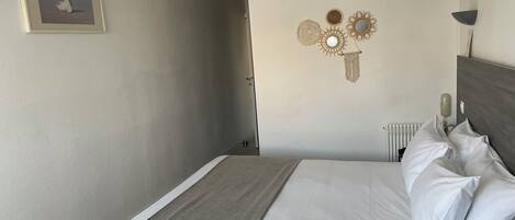 A neatly made bed with white linens and a gray throw, a framed picture on the wall, and decorative wall art.