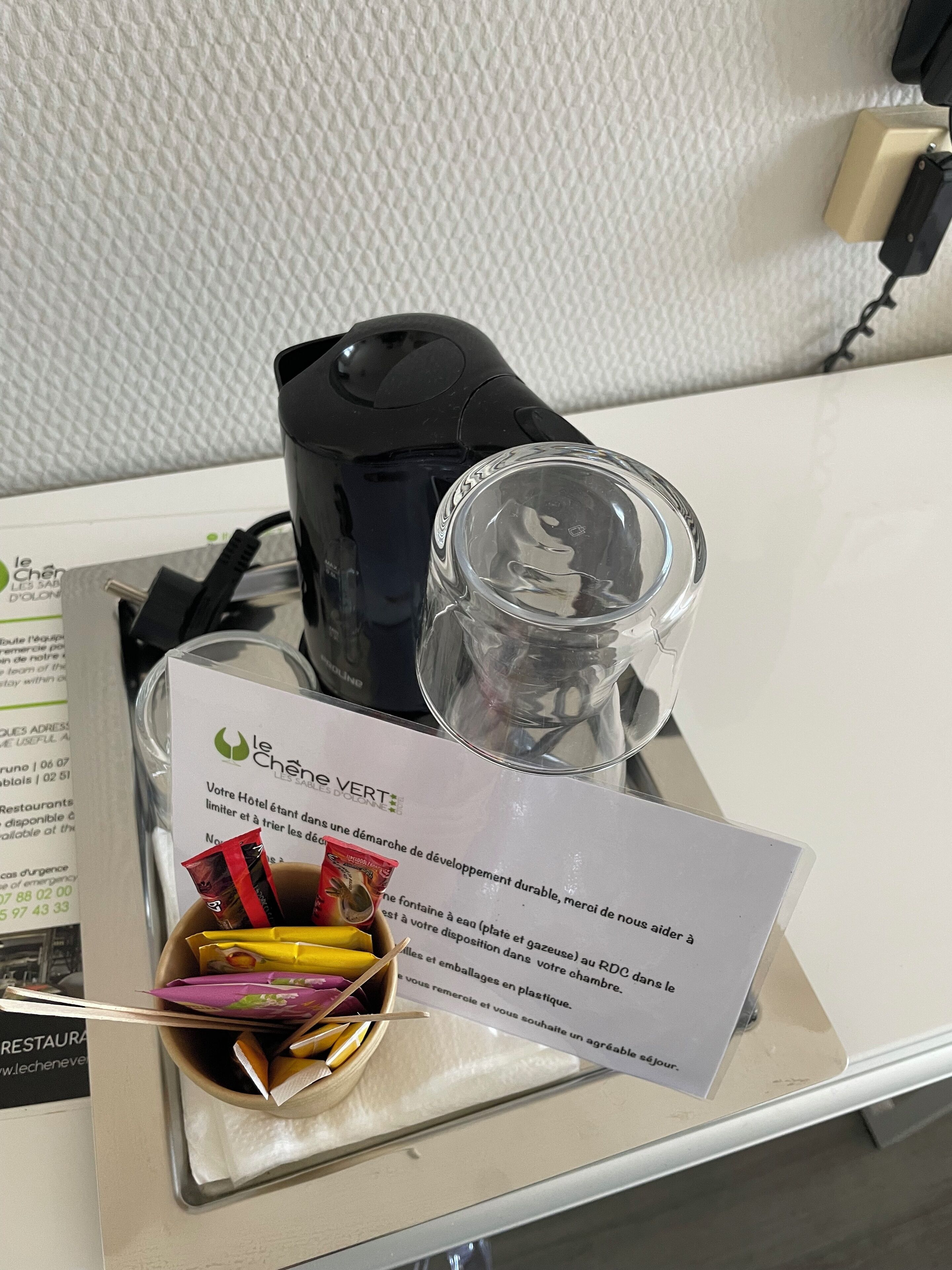 A hotel room with a black coffee maker, a clear glass container, and a menu on the table.