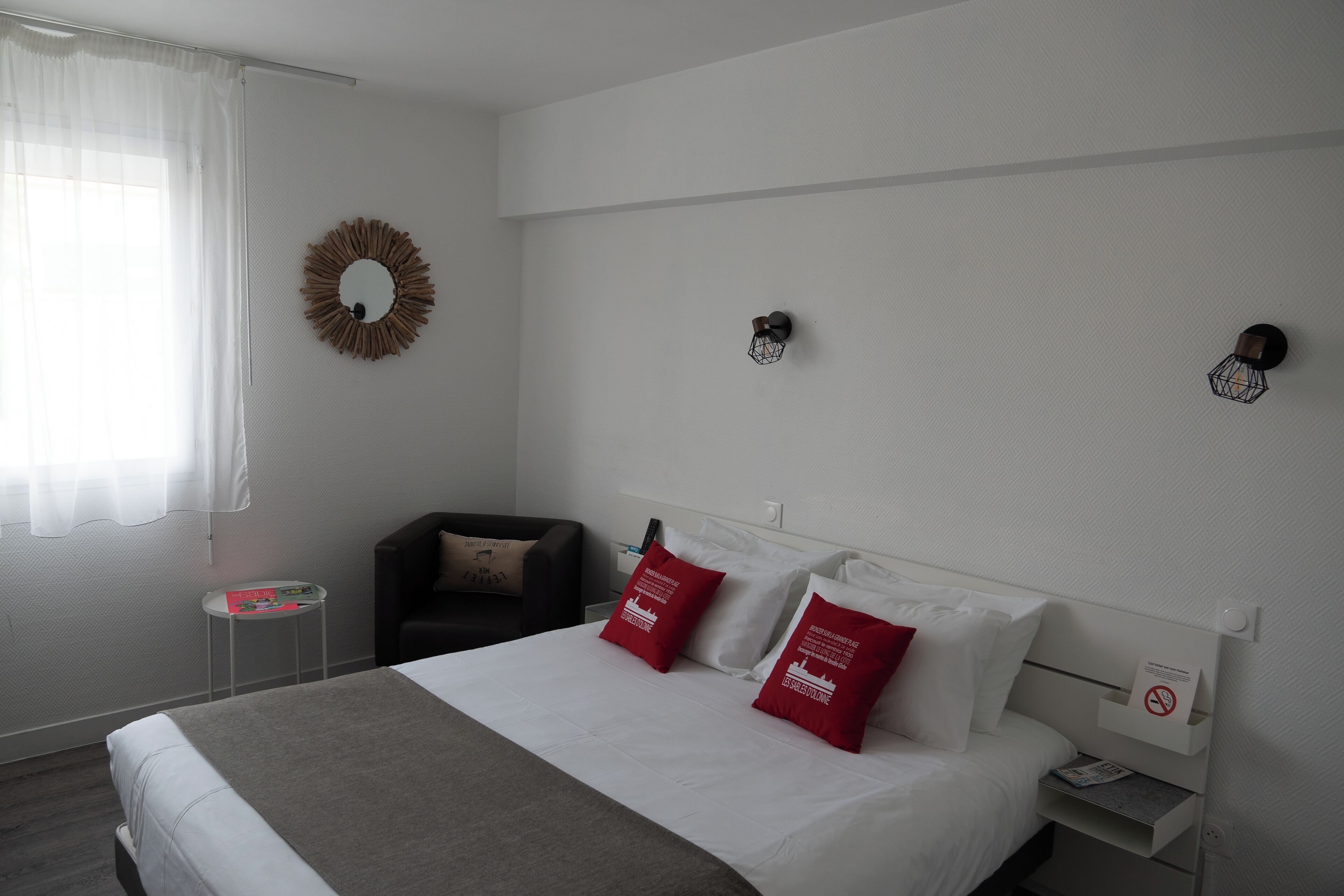 A hotel room with a bed, a small table, a chair, and a wall-mounted light fixture.