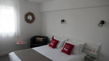 Una habitación de hotel con una cama, una mesita, una silla y una lámpara fijada a la pared.