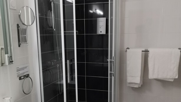 A modern bathroom with a glass-enclosed shower, white sink, and a towel rack. - Citotel Le Chene Vert (Les Sables-d'Olonne)
