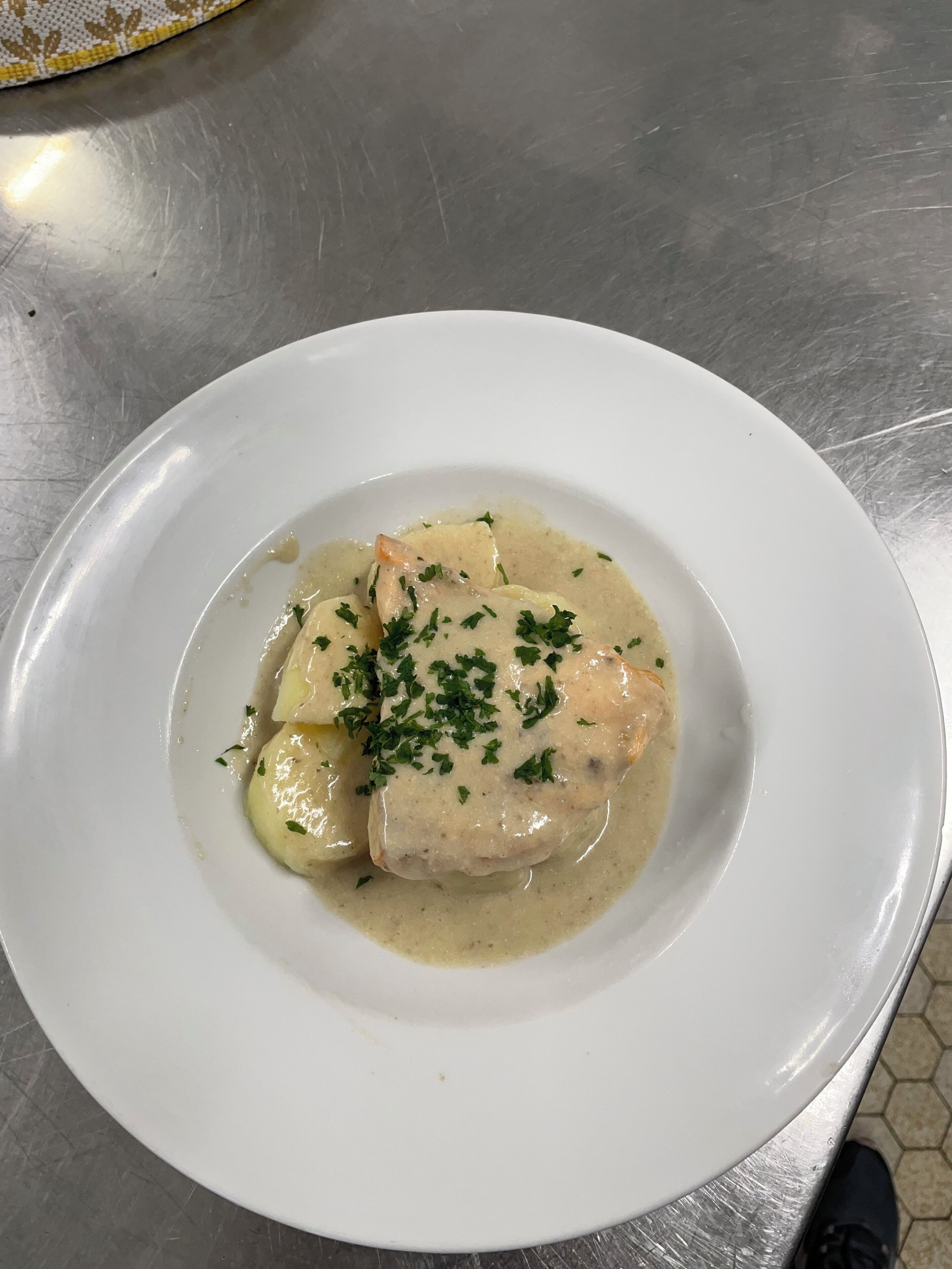 A white plate with a creamy sauce and garnished with chopped herbs, placed on a metallic surface.