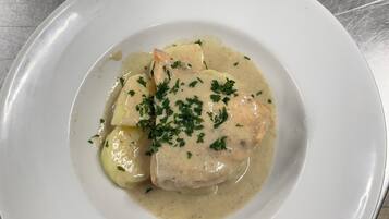 A white plate with a creamy sauce and garnished with chopped herbs, placed on a metallic surface.