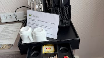 Un mini-bar d’hôtel comprenant une machine à café, un service à thé, des sachets de thé Lipton et un petit plateau avec des condiments.