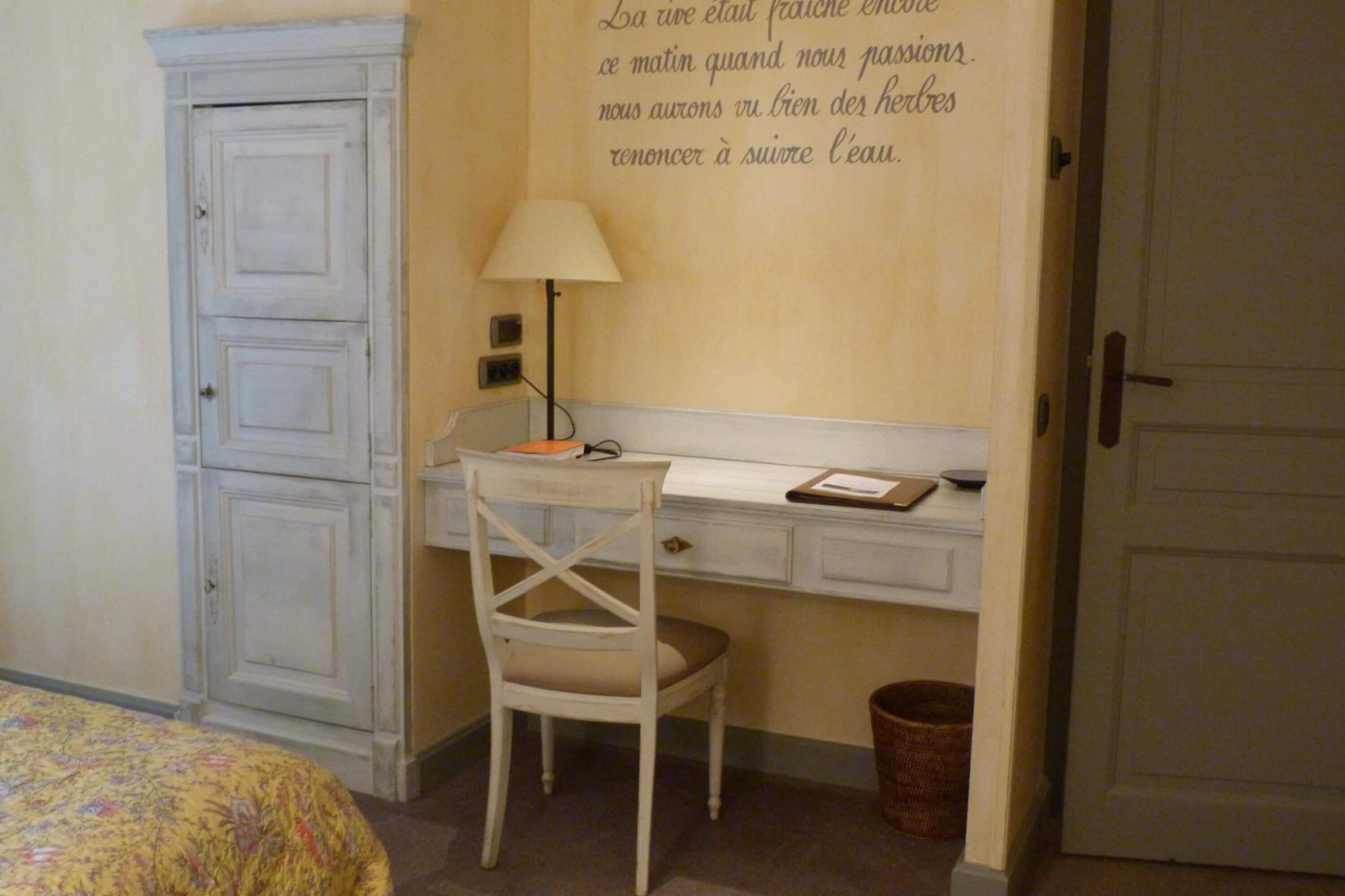 A small room with a desk, chair, and a cabinet. There is a lamp on the desk and a basket on the floor.