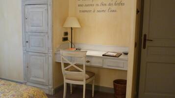 Une petite pièce comprenant un bureau, une chaise et un placard. Il y a une lampe sur le bureau et un panier sur le sol.