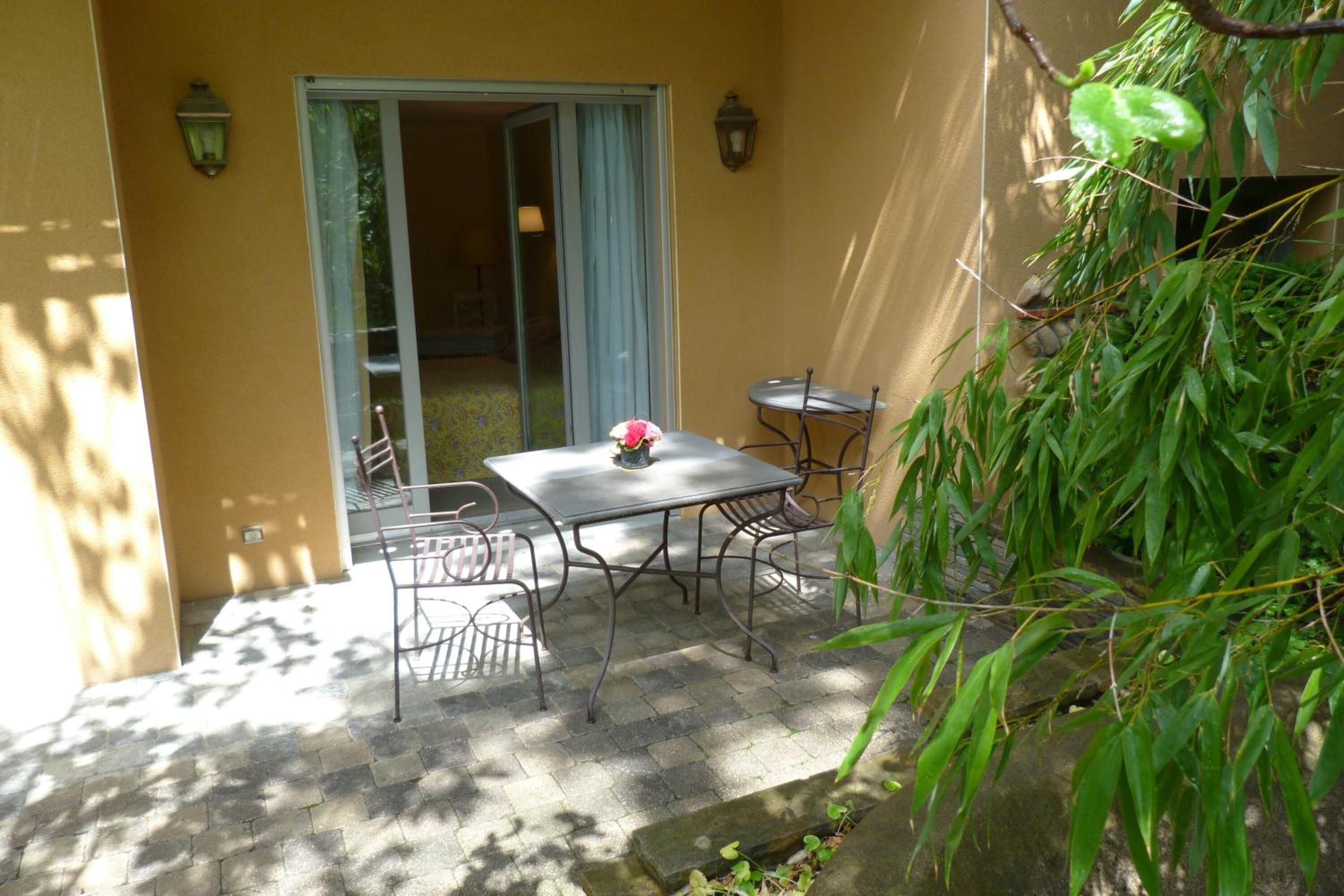 Une terrasse avec une table et des chaises, une porte-fenêtre coulissante et un petit jardin agrémenté d’un plant de bambou.