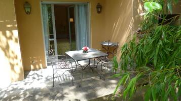 Une terrasse avec une table et des chaises, une porte-fenêtre coulissante et un petit jardin agrémenté d’un plant de bambou.
