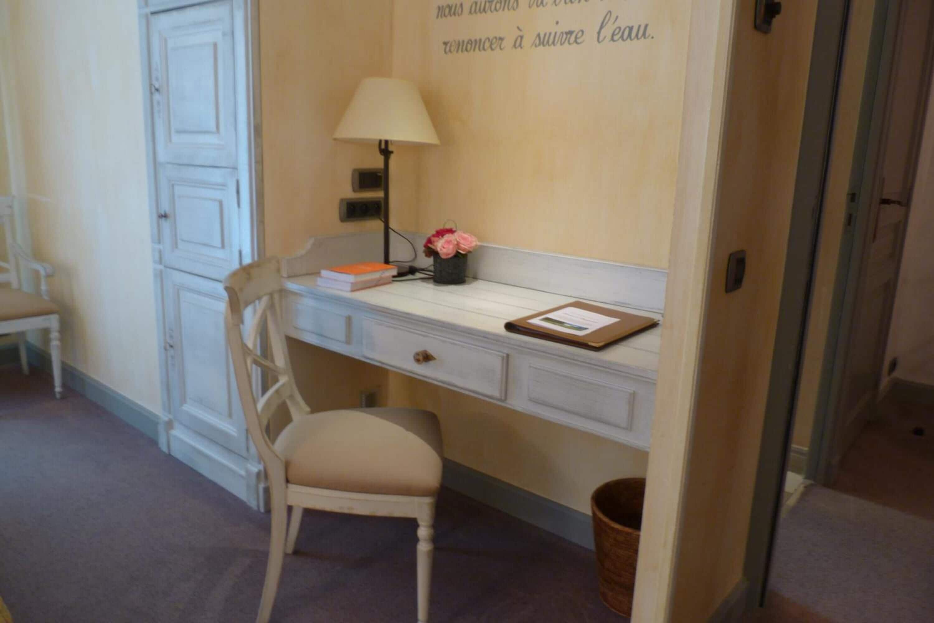 A study room with a desk, chair, lamp, and a wall with a French quote.