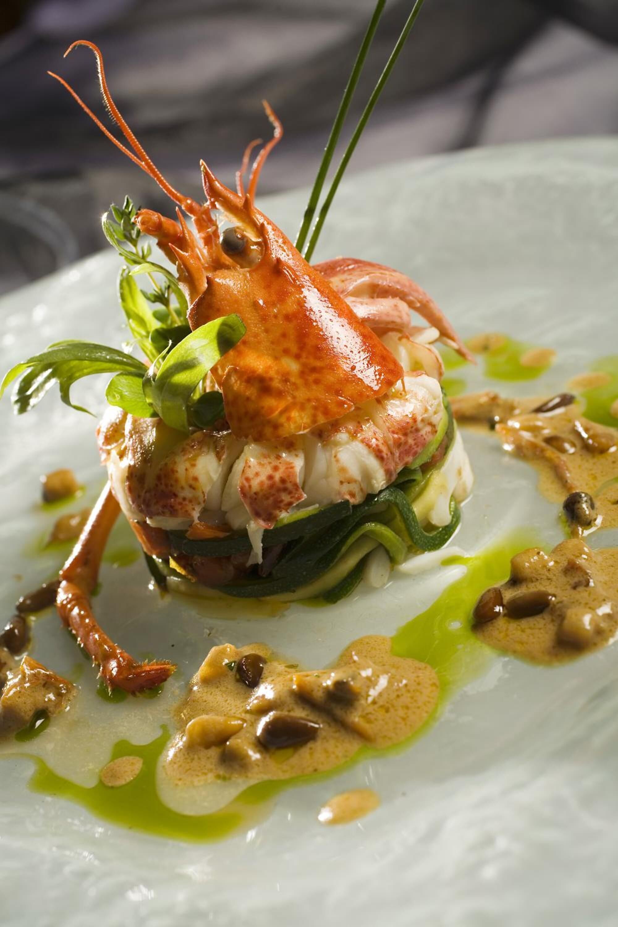 A lobster dish on a plate with green sauce and a creamy sauce.