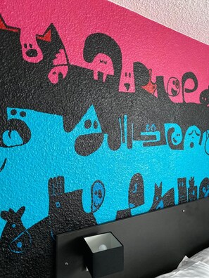 Una habitación con una cama, una mesita de noche y una pared decorada con arte abstracto y colorido.
