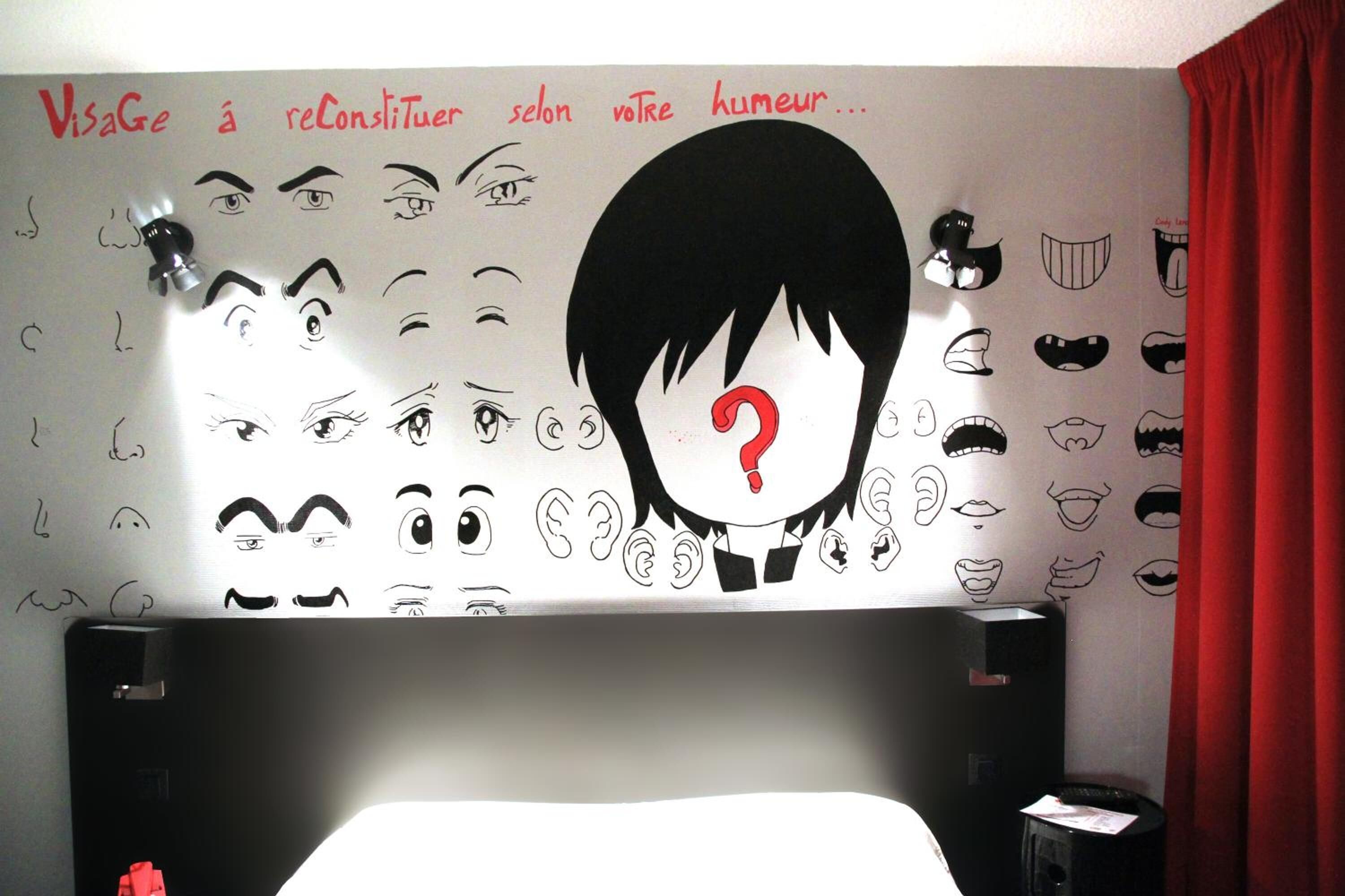 A bedroom with a bed, a wall with various facial expressions, and a red curtain.