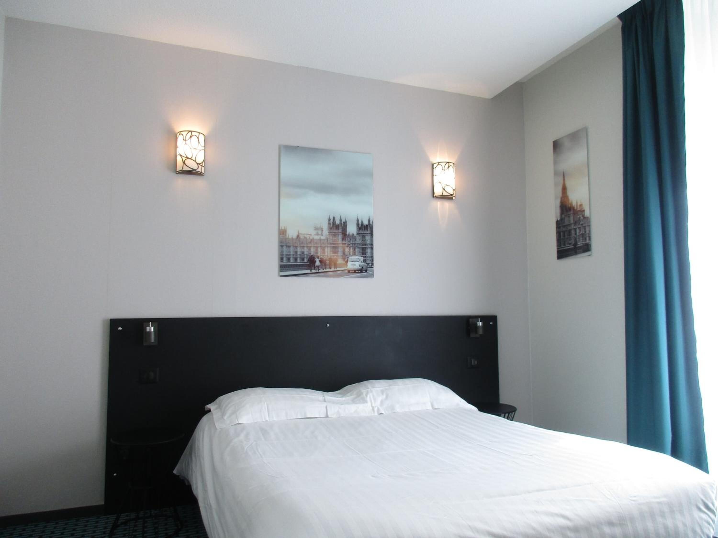 Una habitación de hotel con una cama grande, dos lámparas de pared y dos cuadros con imágenes de monumentos de Londres.